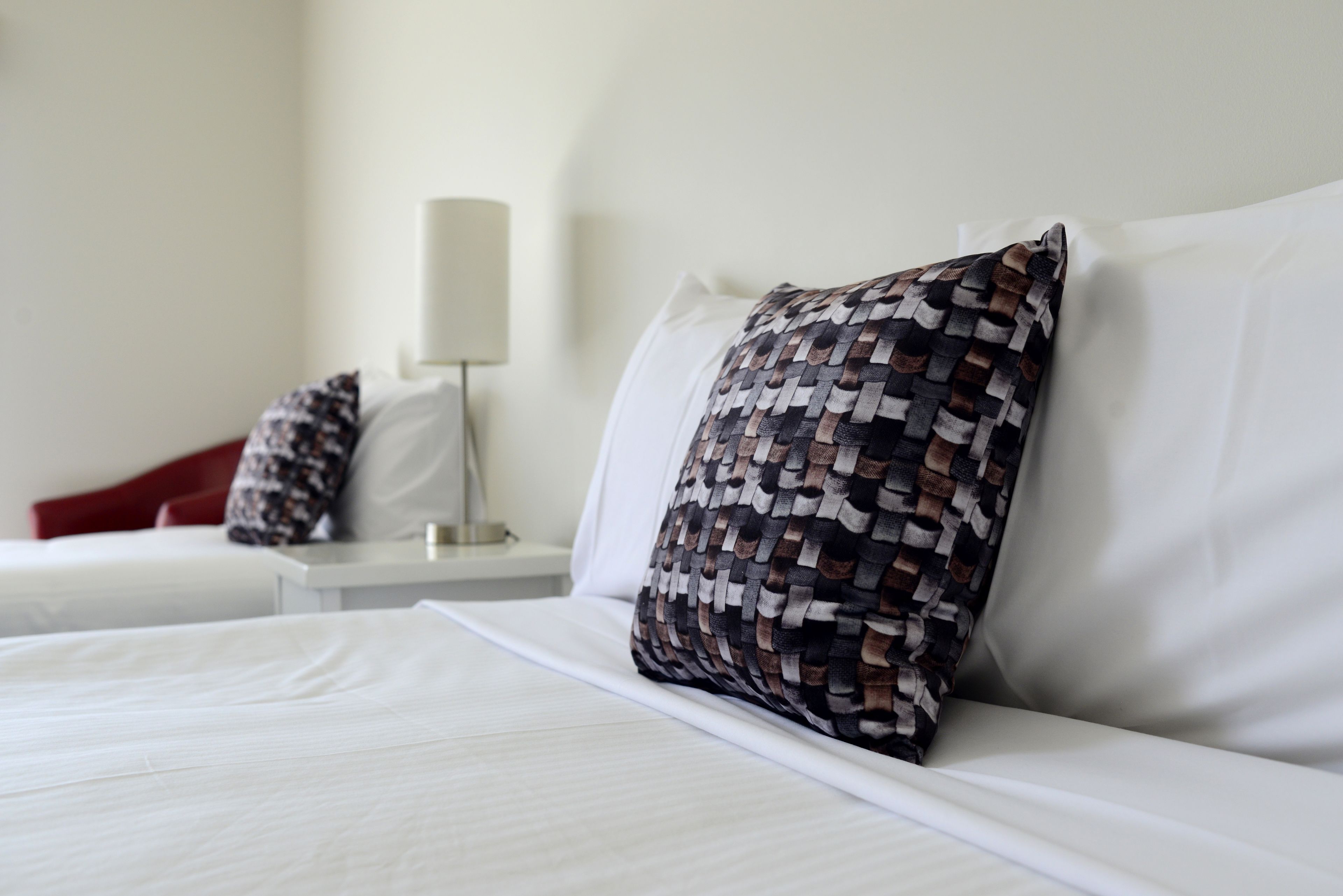 A neatly made bed with white linens and a patterned pillow.