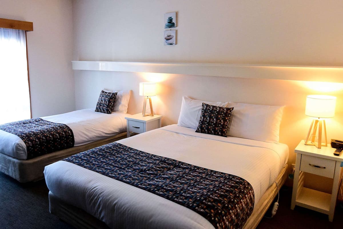 Habitación de hotel con dos camas, cada una con una almohada y una mesita de noche con lámpara.