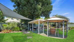 Ein Garten mit zwei überdachten Terrassen, einem Grill und einem Holzfass.