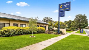 Ein Comfort Inn Benalla mit einem gepflegten Rasen, blauem Himmel und einem Schild, das Einrichtungen wie Hallenbad und Grillplatz anzeigt.