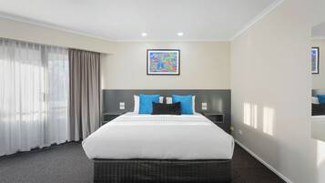 Habitación de hotel con una cama grande, dos mesitas de noche, un cabecero y una ventana con cortinas.