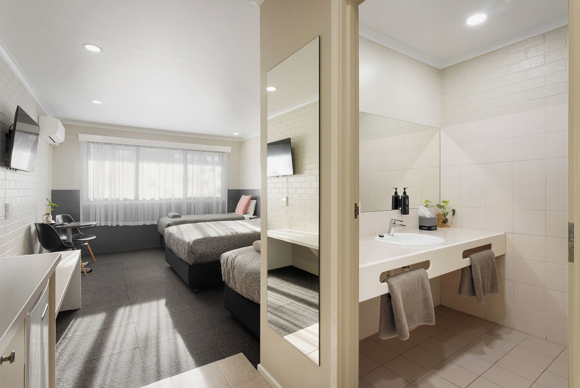 A hotel room with a bed, a desk, a chair, a TV, a bathroom with a sink and mirror, and a window with curtains.