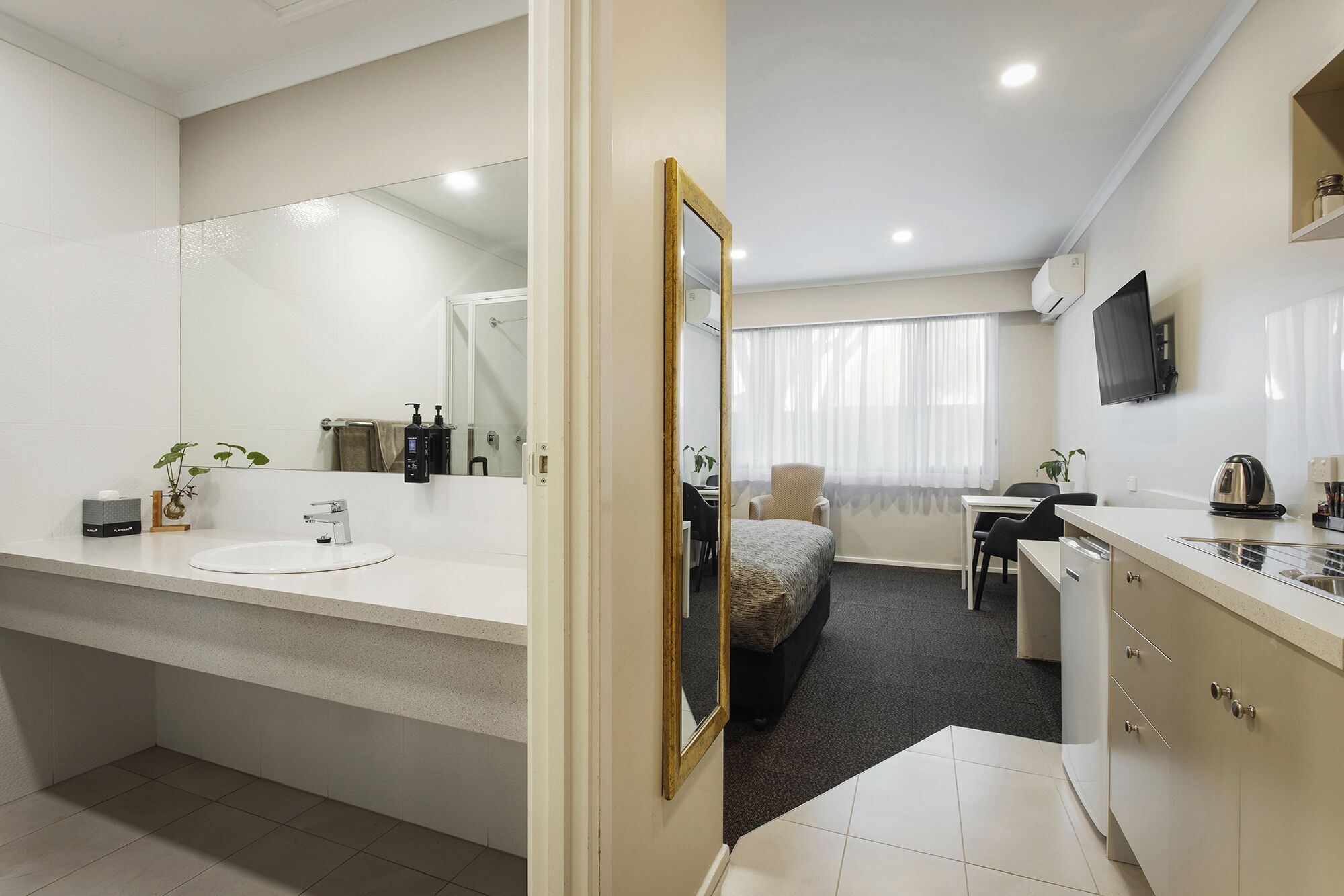 Habitación de hotel con baño, cama, escritorio y televisor.