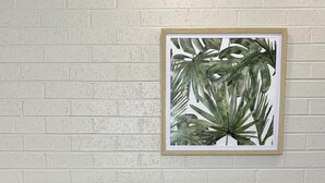 A hotel room with a white brick wall, a framed botanical print, a bed with white and green pillows, and a dark nightstand with a power outlet. - Bendigo Central Deborah (Bendigo)