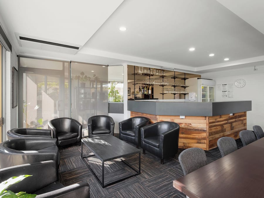 Un espace de détente moderne avec des fauteuils en cuir, un comptoir de bar et une vue à travers une porte vitrée.