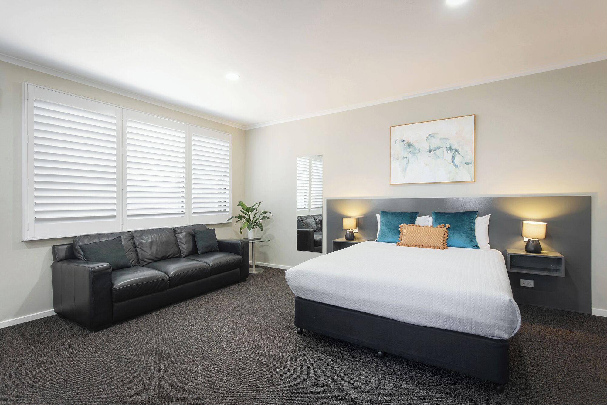 A hotel room with a bed, a sofa, a nightstand, a lamp, and a painting on the wall.