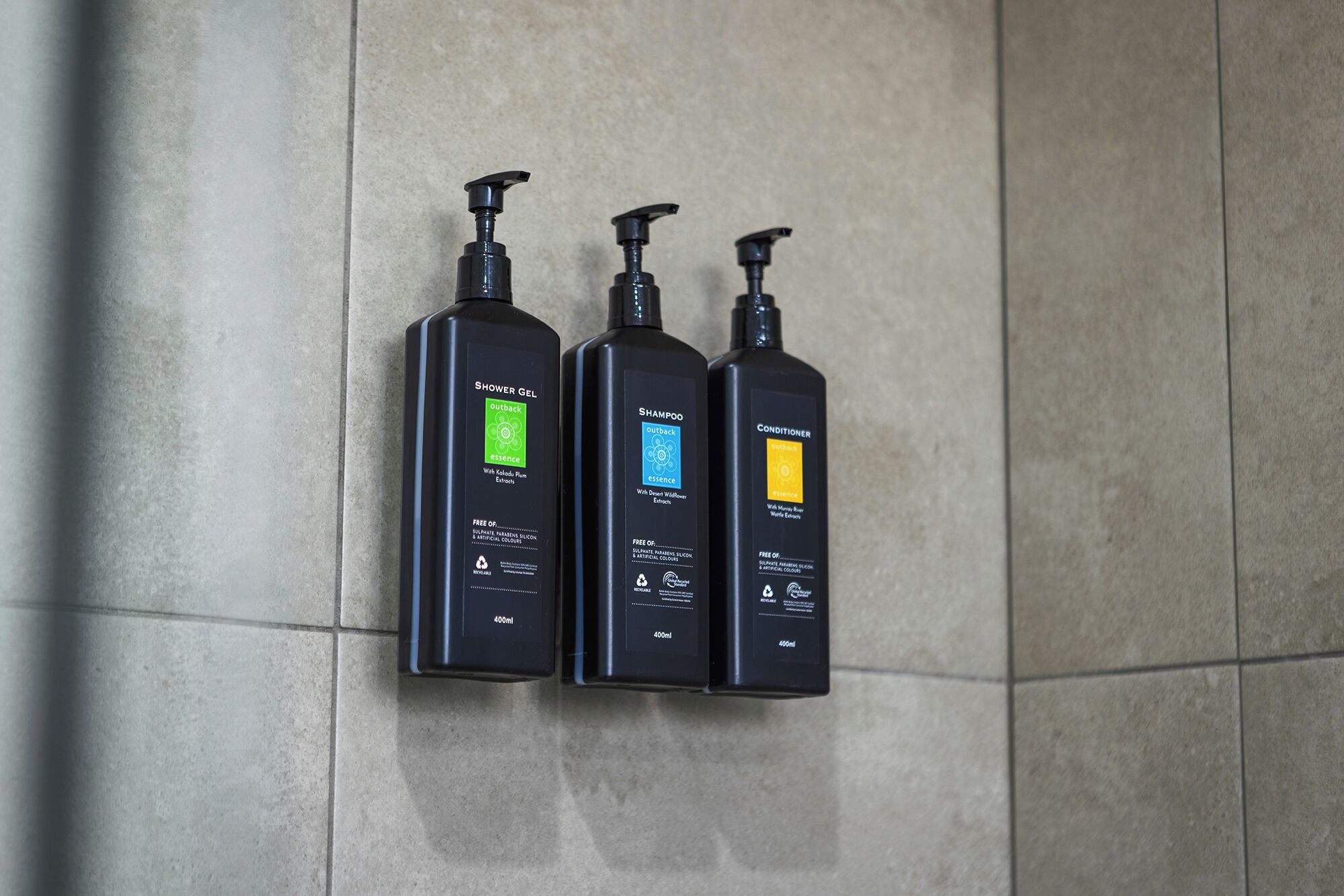 Three black bottles of Outback Essence products on a tiled wall.