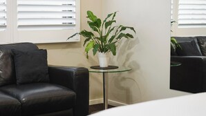 A room with a black leather sofa, a glass table with a white plant, and white blinds on the windows. - Bendigo Central Deborah (Bendigo)