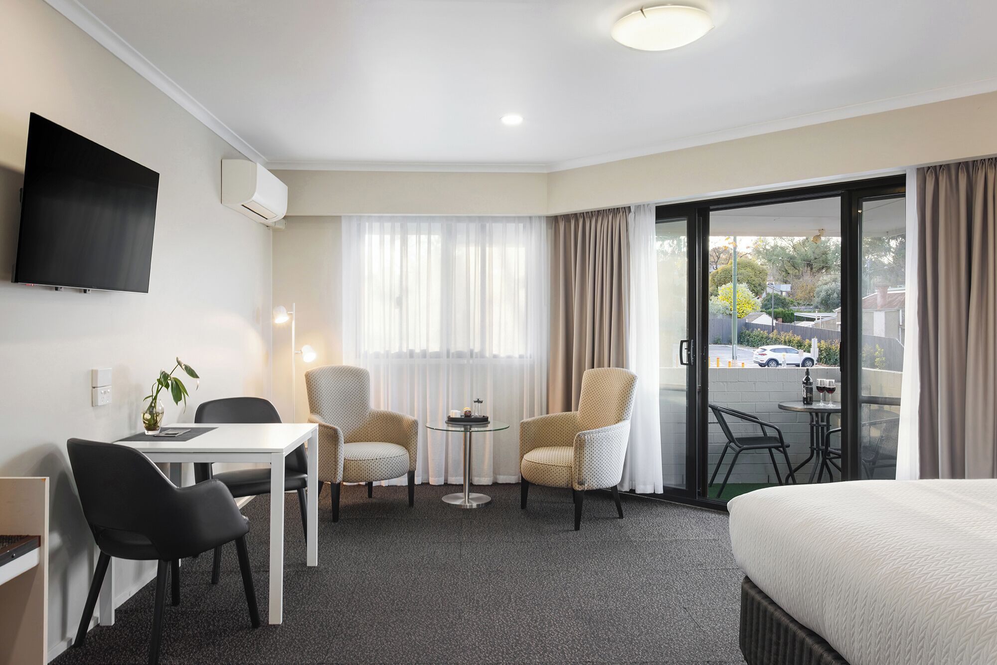 Habitación de hotel con cama, escritorio con sillas, televisor, pequeña mesa con una silla y vistas al exterior.
