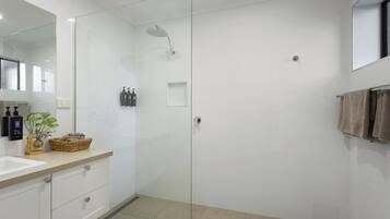Ein modernes Badezimmer mit einer Duschkabine aus Glas, einem weißen Waschbecken und einem Spiegel.