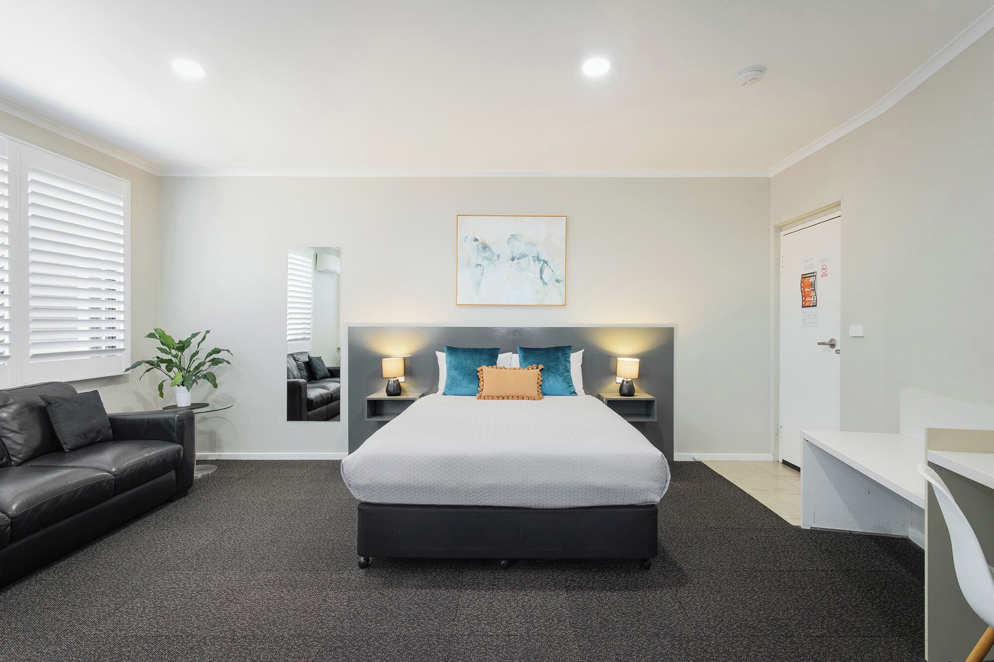 Quarto de hotel com cama, escrivaninha, cadeira, sofá e planta em vaso.