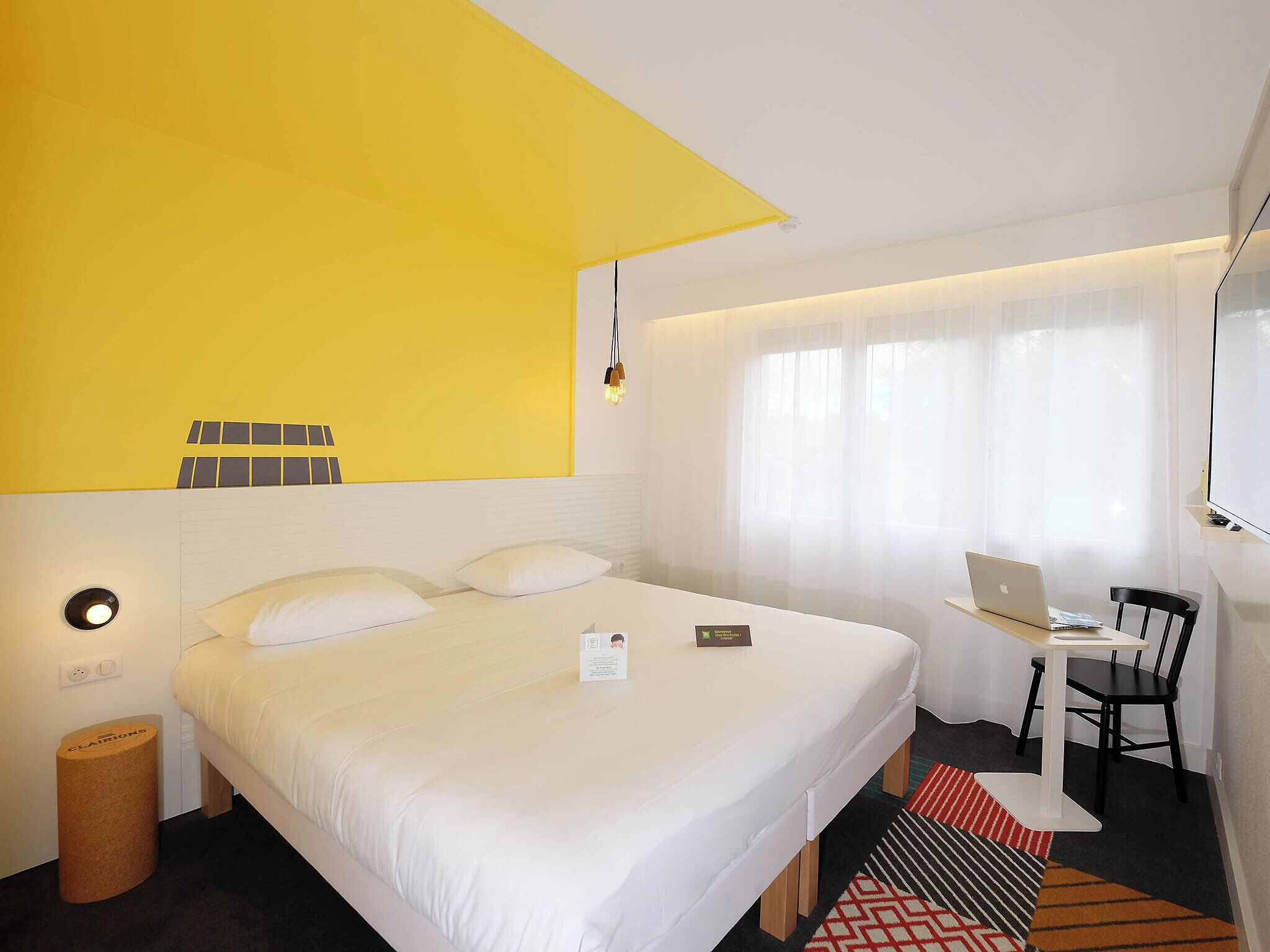 Habitación de hotel con cama, escritorio, laptop, silla y ventana con cortinas.