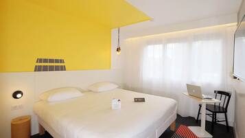 Habitación de hotel con cama, escritorio, laptop, silla y ventana con cortinas.
