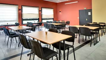 A conference room with multiple tables and chairs, large windows with blinds, and a door with an exit sign.