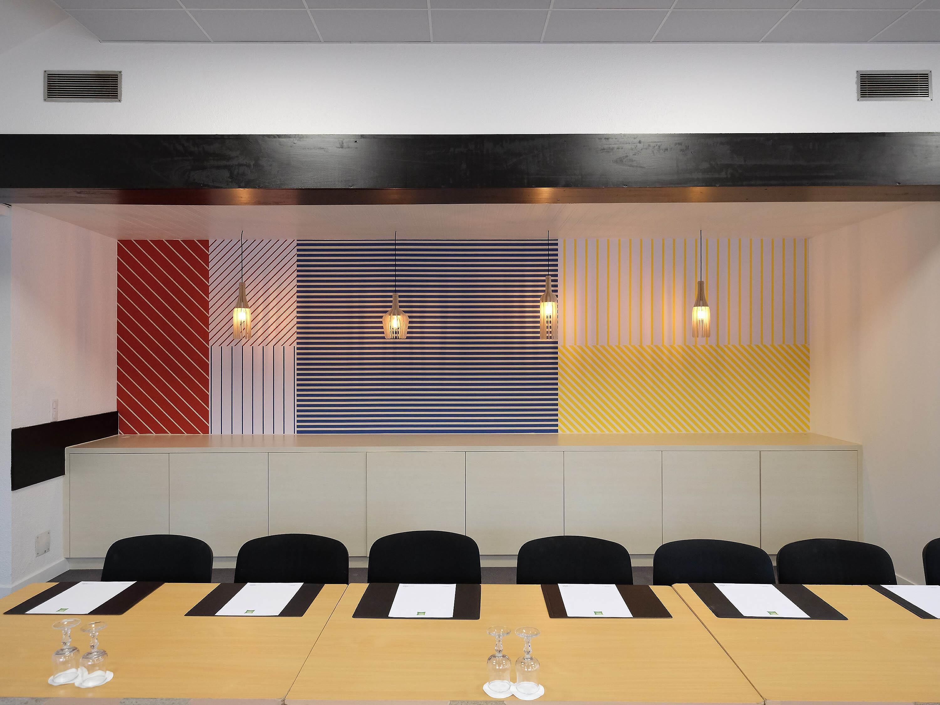 Une salle de conférence avec une longue table, des chaises noires et un mur orné de motifs.