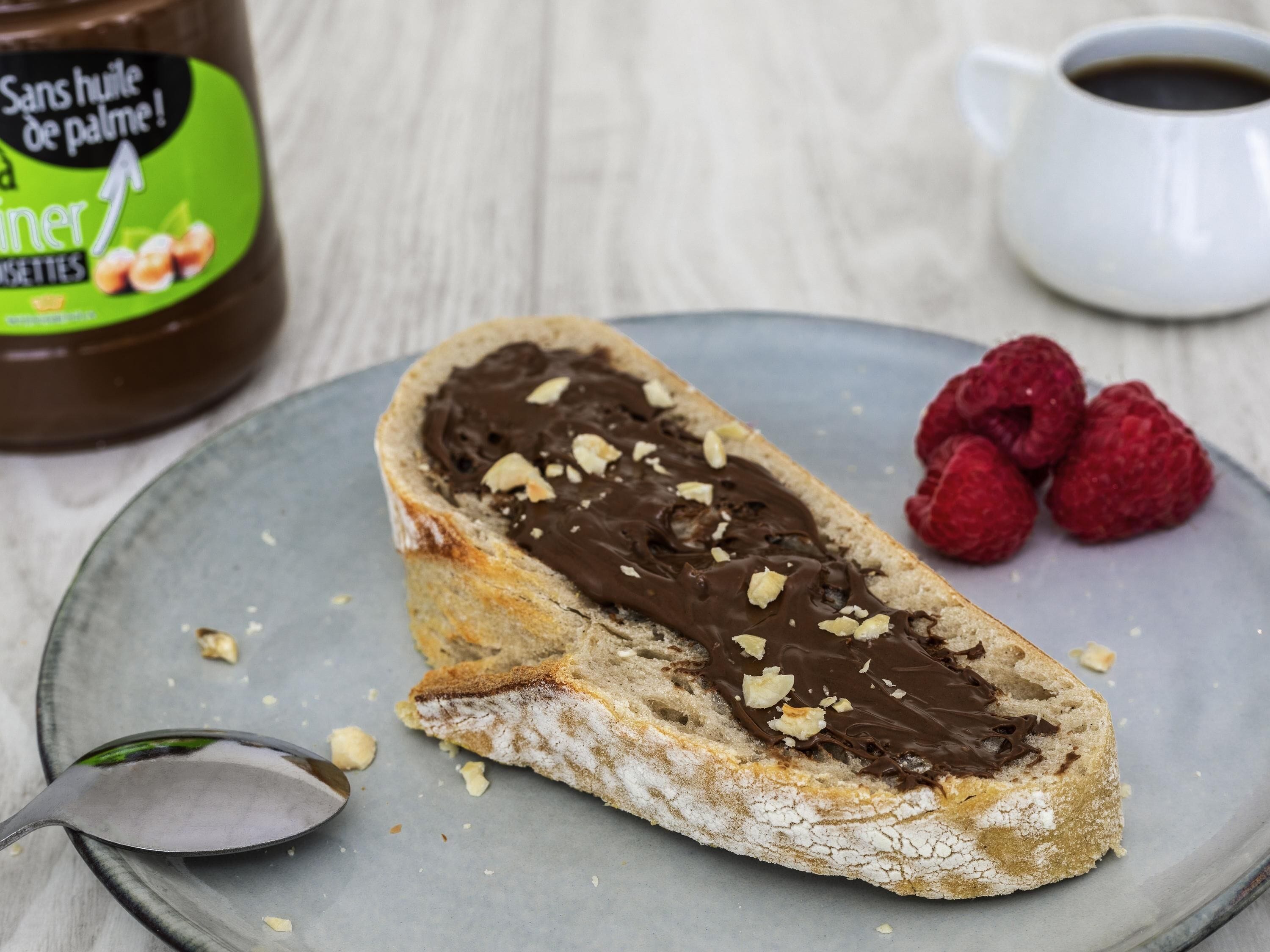 A dessert with chocolate spread and almonds, a jar of chocolate spread, and a cup of coffee on a table.