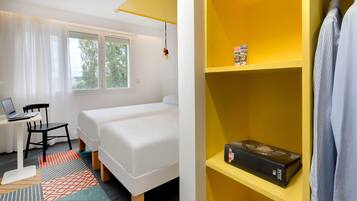 A hotel room with two beds, a desk with a laptop, a chair, and a bookshelf with a book.