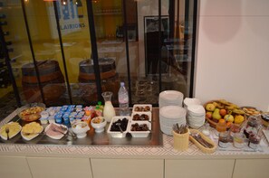 Un bufé con diversas opciones de comida y bebidas, como frutas, yogur y una selección de refrescos.