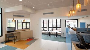 Un espace de bureau moderne comprenant un bureau, un ordinateur et une chaise, de grandes fenêtres et des luminaires suspendus.