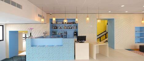 A modern bar area with a counter, shelves of bottles, and hanging lights.