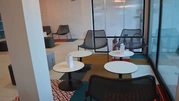 Un intérieur moderne avec un espace salon comprenant des tables et des chaises rondes, un sol à motifs et une grande fenêtre équipée de stores.