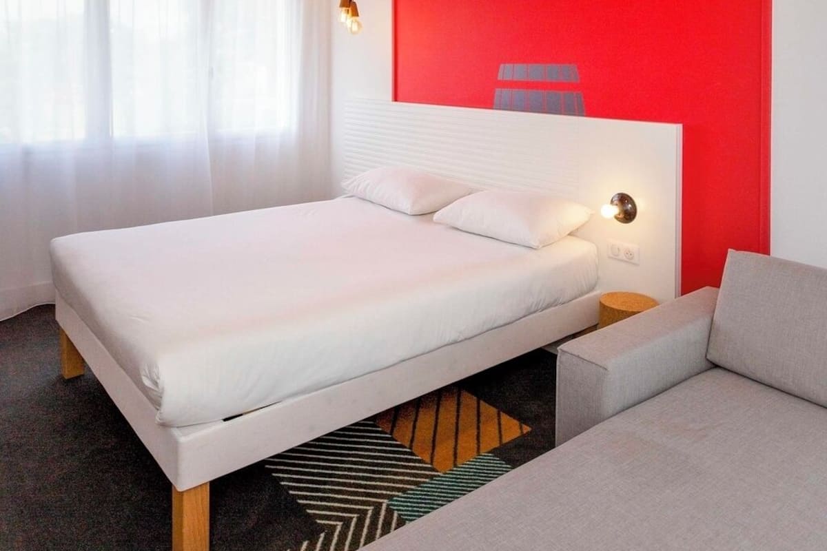 Ein Schlafzimmer mit Bett, Nachttisch, einer Couch und einer roten Akzentwand.