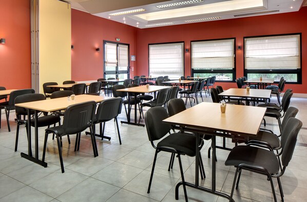 A conference room with multiple tables and chairs, large windows with blinds, and a red wall.