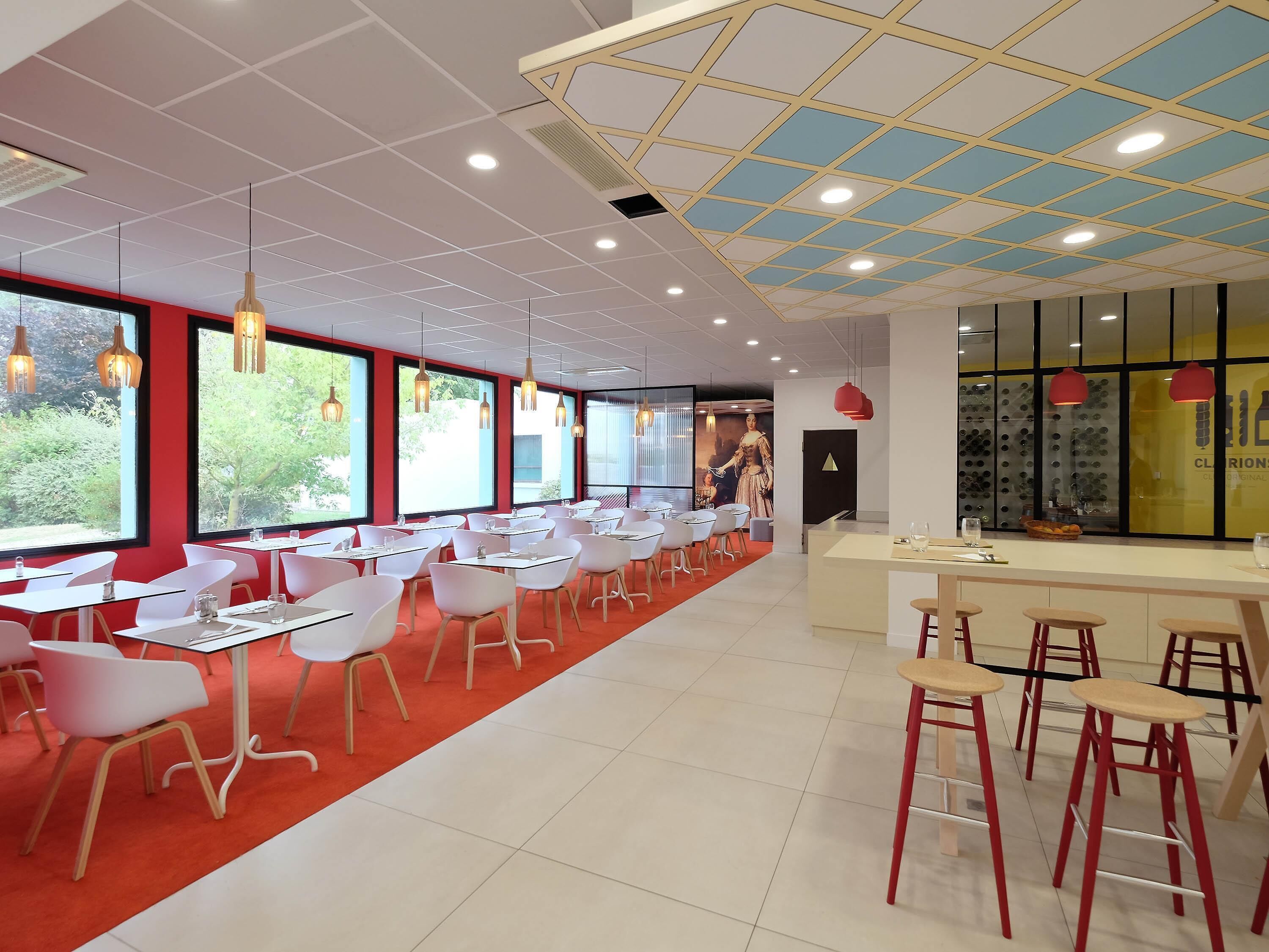 Un interior de restaurante moderno con mesas blancas, sillas rojas y una alfombra roja.