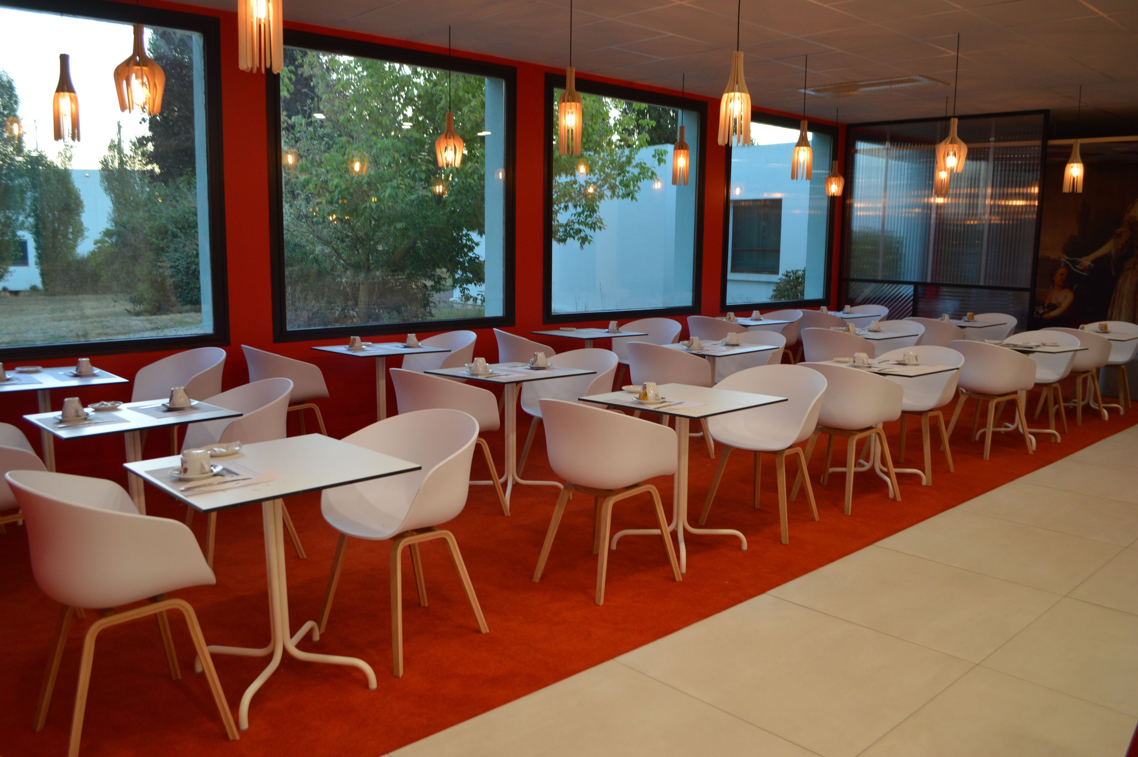 Un restaurante con sillas y mesas blancas, ventanas amplias y lámparas colgantes.