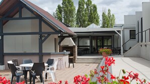 Une terrasse extérieure avec des tables et des chaises, un espace barbecue et un bâtiment doté d’un toit en pente.