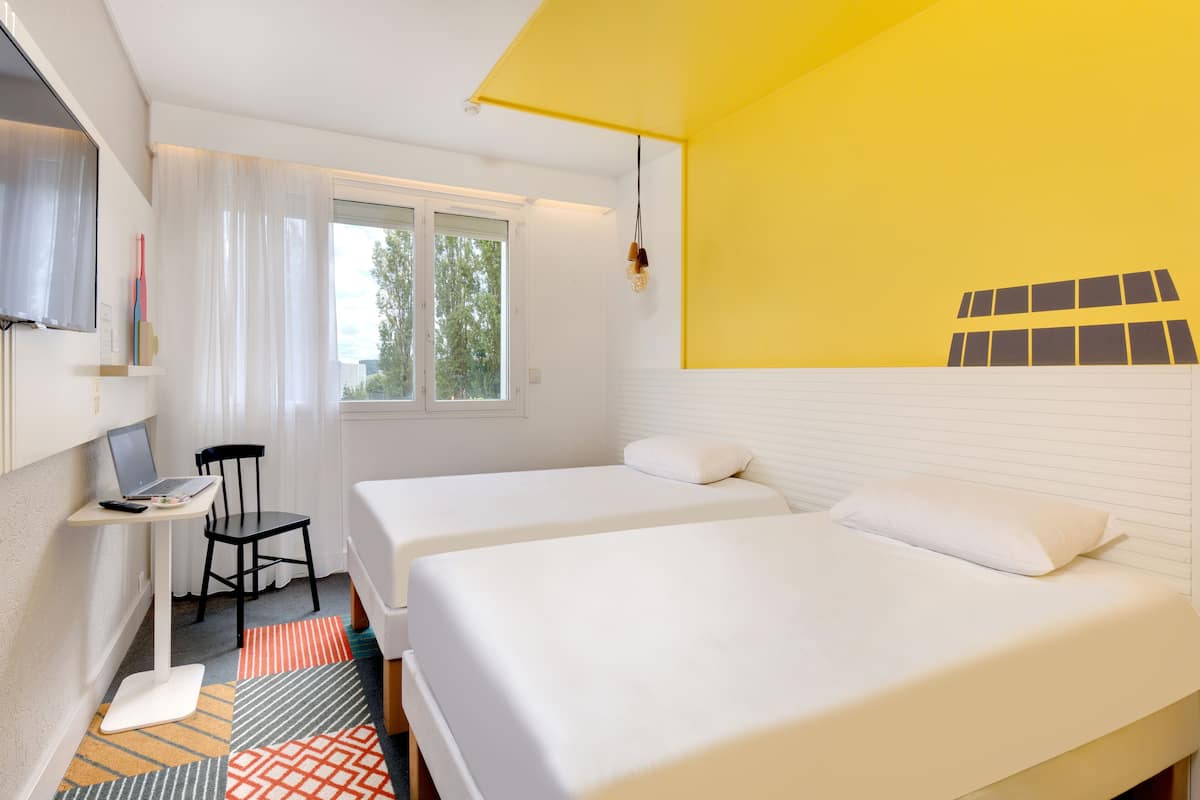 Ein Zimmer mit zwei Betten, einem Schreibtisch mit einem Laptop und einem Stuhl.