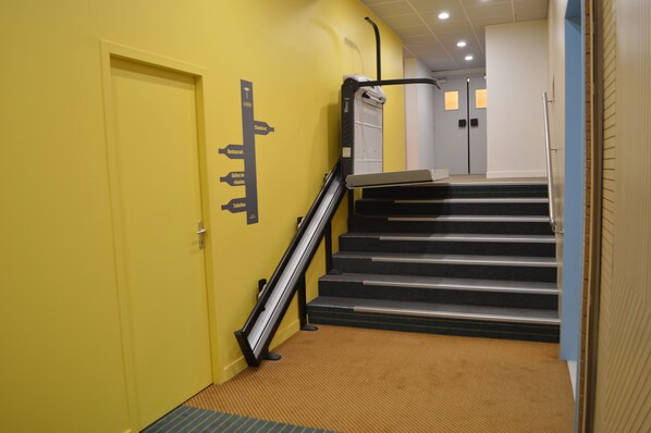 Una escalera con barandilla, escalones alfombrados y una pared amarilla con una señal indicativa.