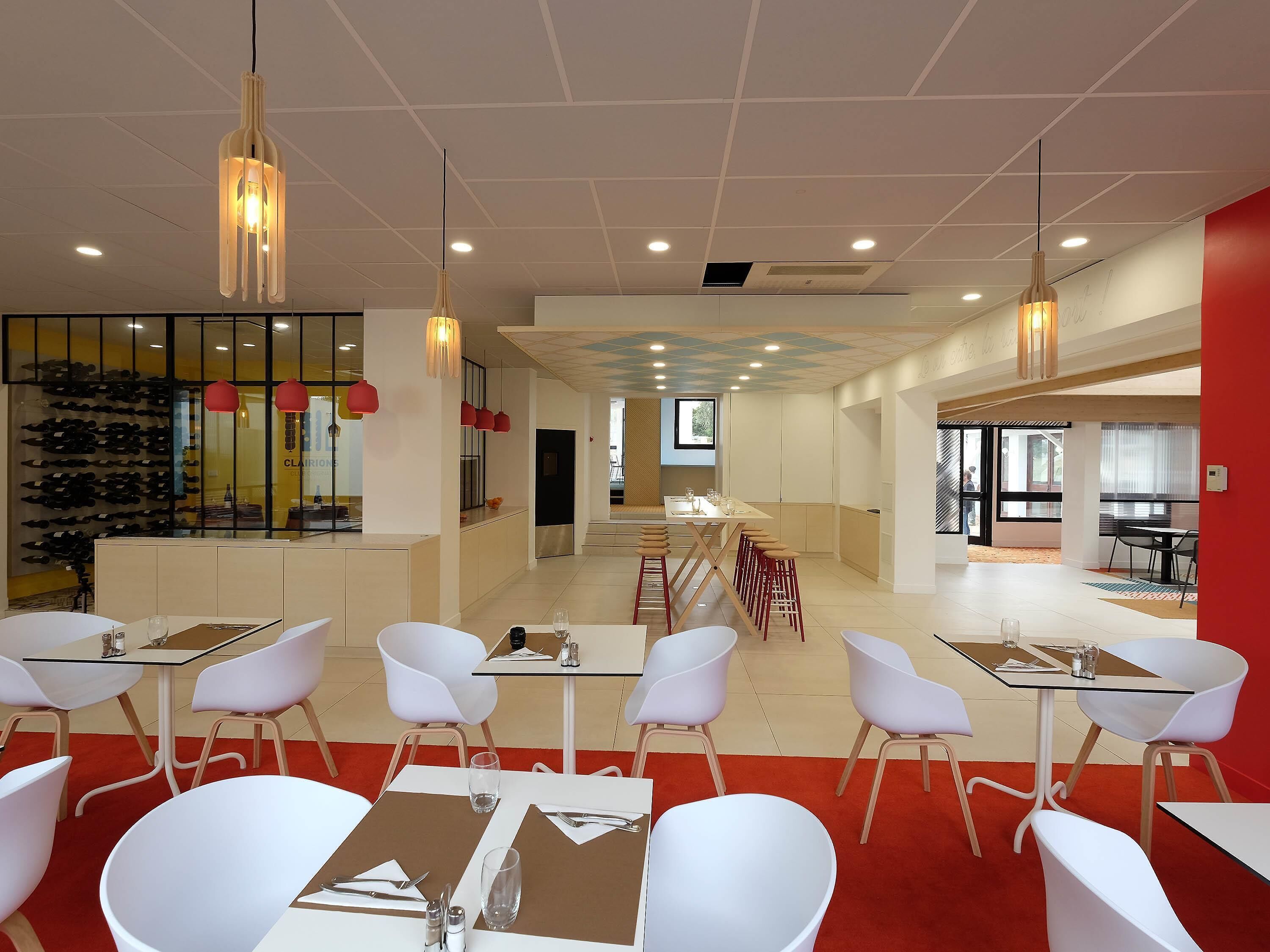 Un comedor moderno con mesas y sillas blancas, detalles en rojo e iluminación colgante.