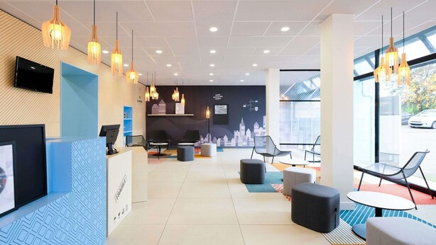 Un hall d’hôtel moderne doté d’un comptoir d’accueil, d’un espace salon et de grandes fenêtres donnant sur l’extérieur.