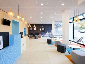 A modern hotel lobby with a reception desk, seating area, and large windows offering a view of the outside.