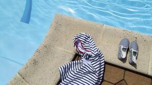 Un espace aménagé au bord de la piscine, avec un fauteuil de relaxation, une serviette à rayures et une paire de chaussons à rayures.