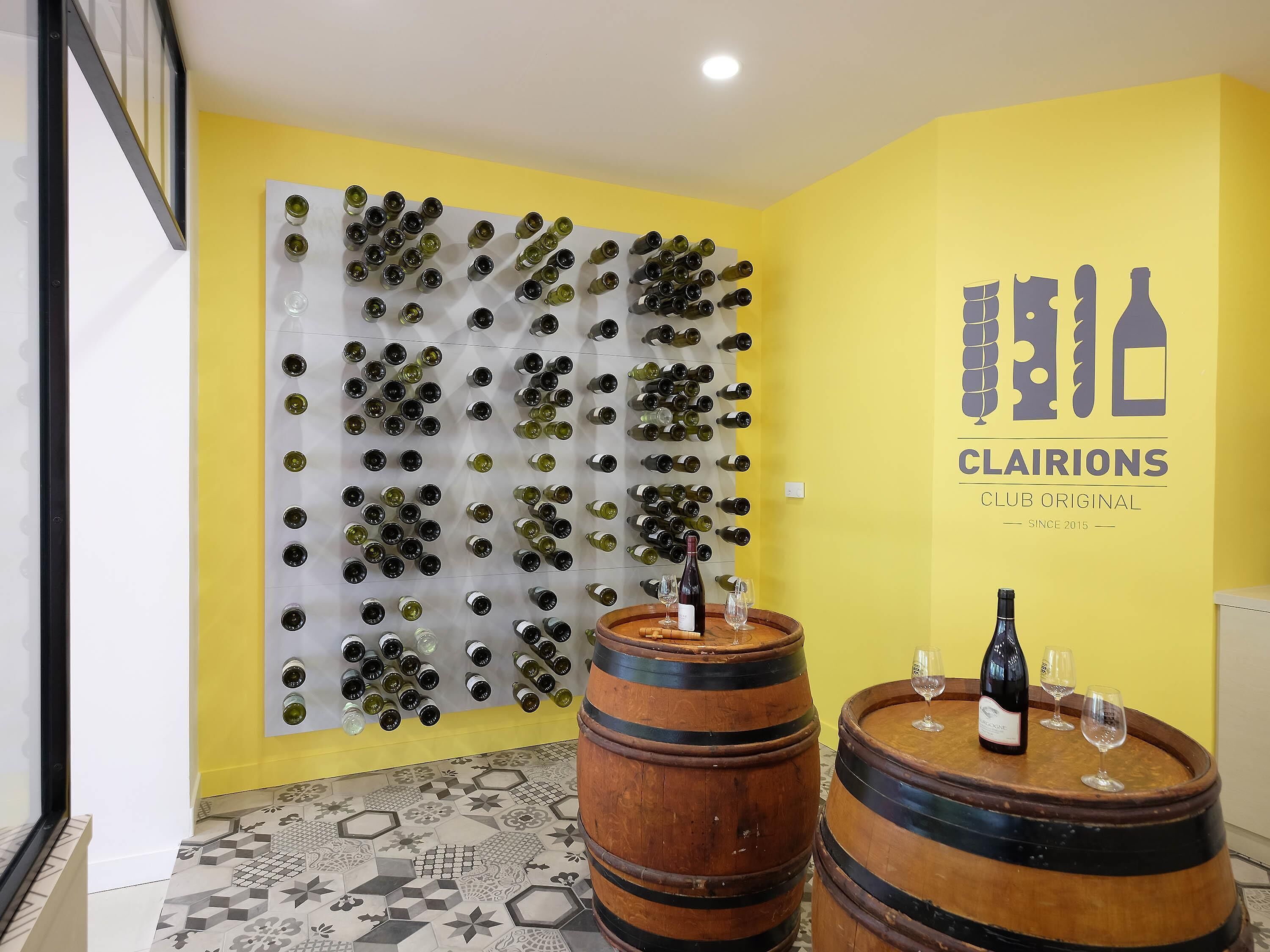 Een kamer met een wandmontage wijnrek, houten vaten en een logo voor 'CLAIRIONS CLUB ORIGINAL' op de muur.
