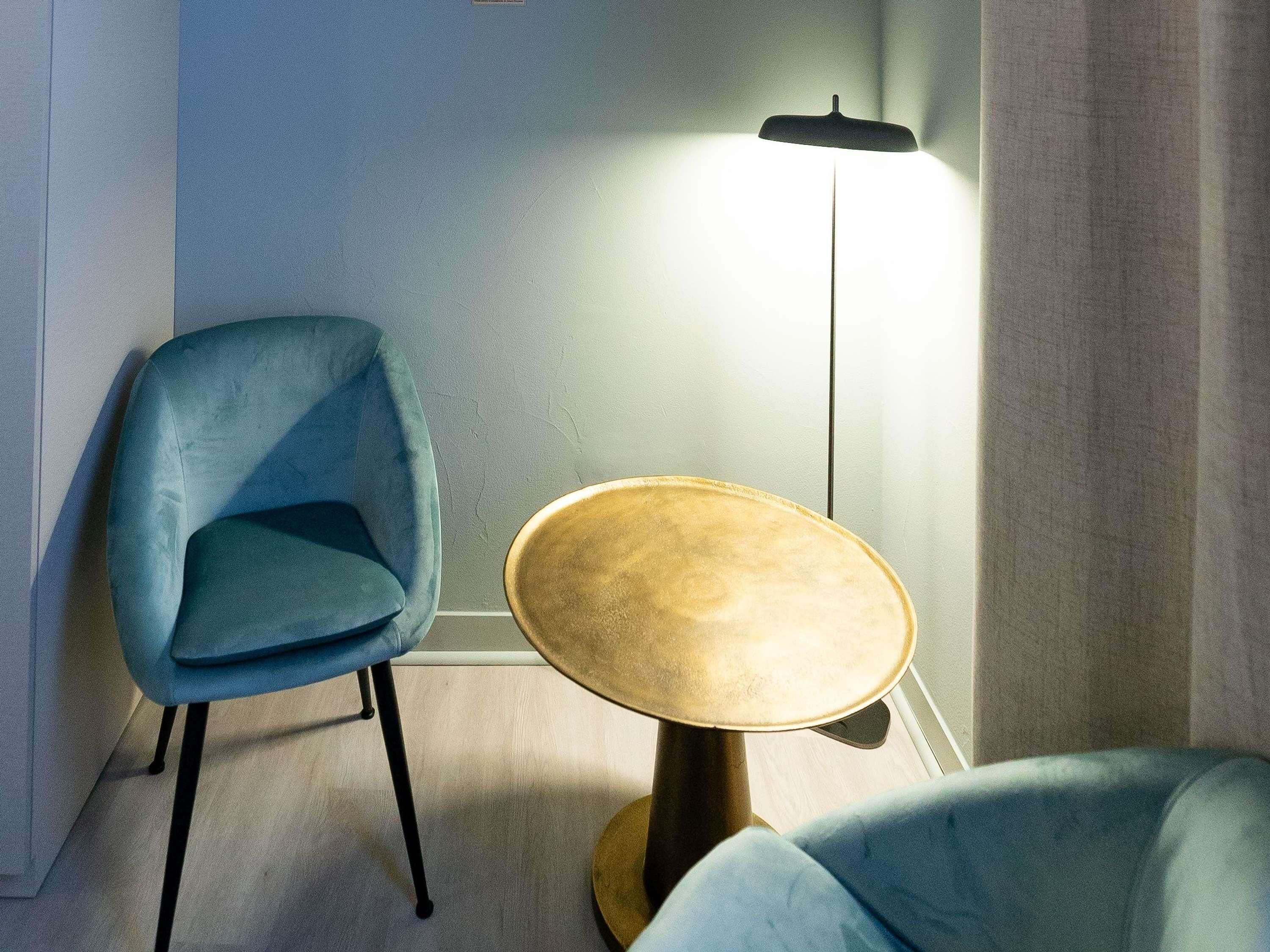 Een kamer met een blauwe fauteuil, een ronde houten tafel en een vloerlamp.