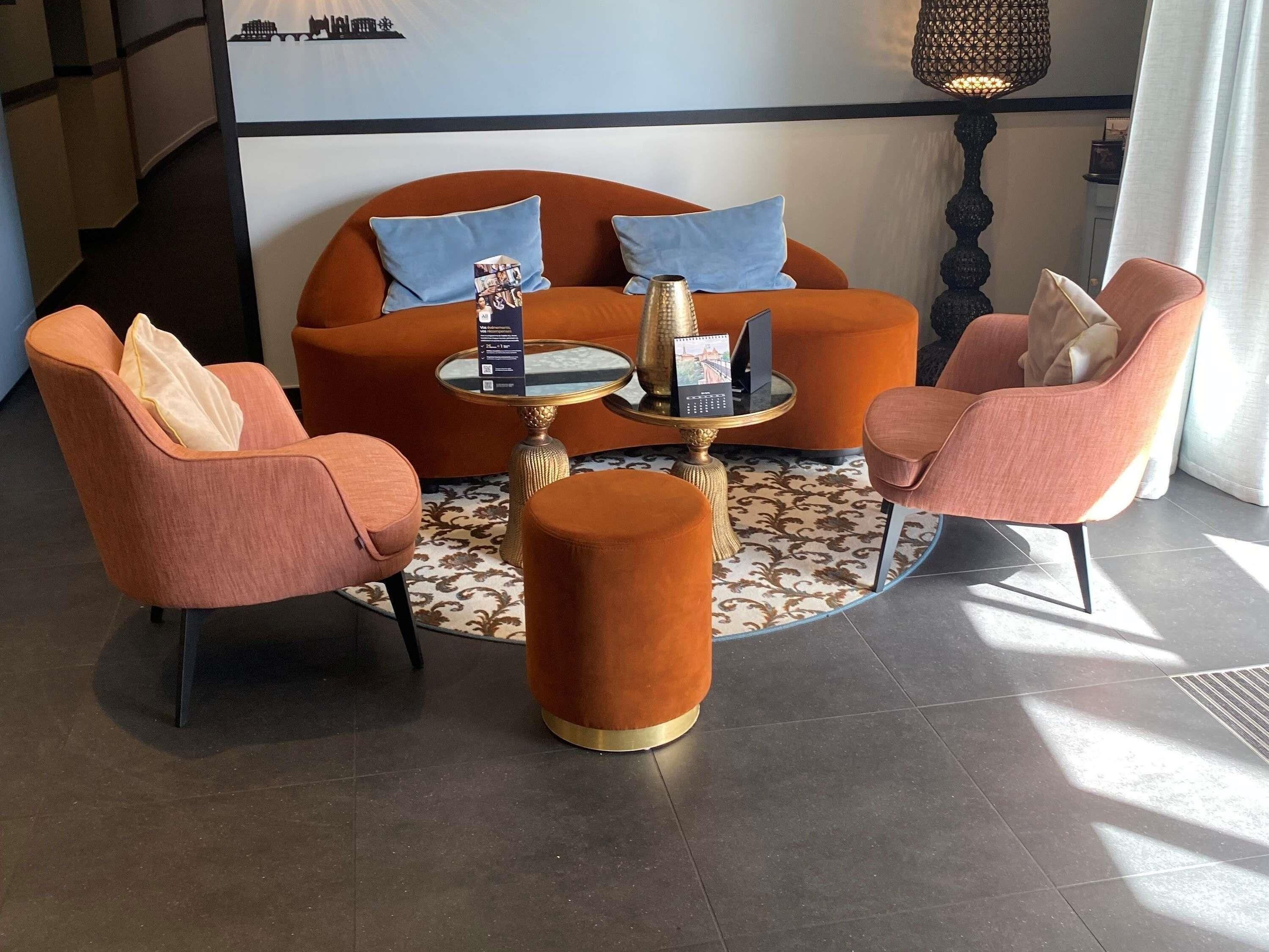 Een moderne zithoek met een bank, twee fauteuils, een rond bijzettafeltje en een decoratieve lamp.