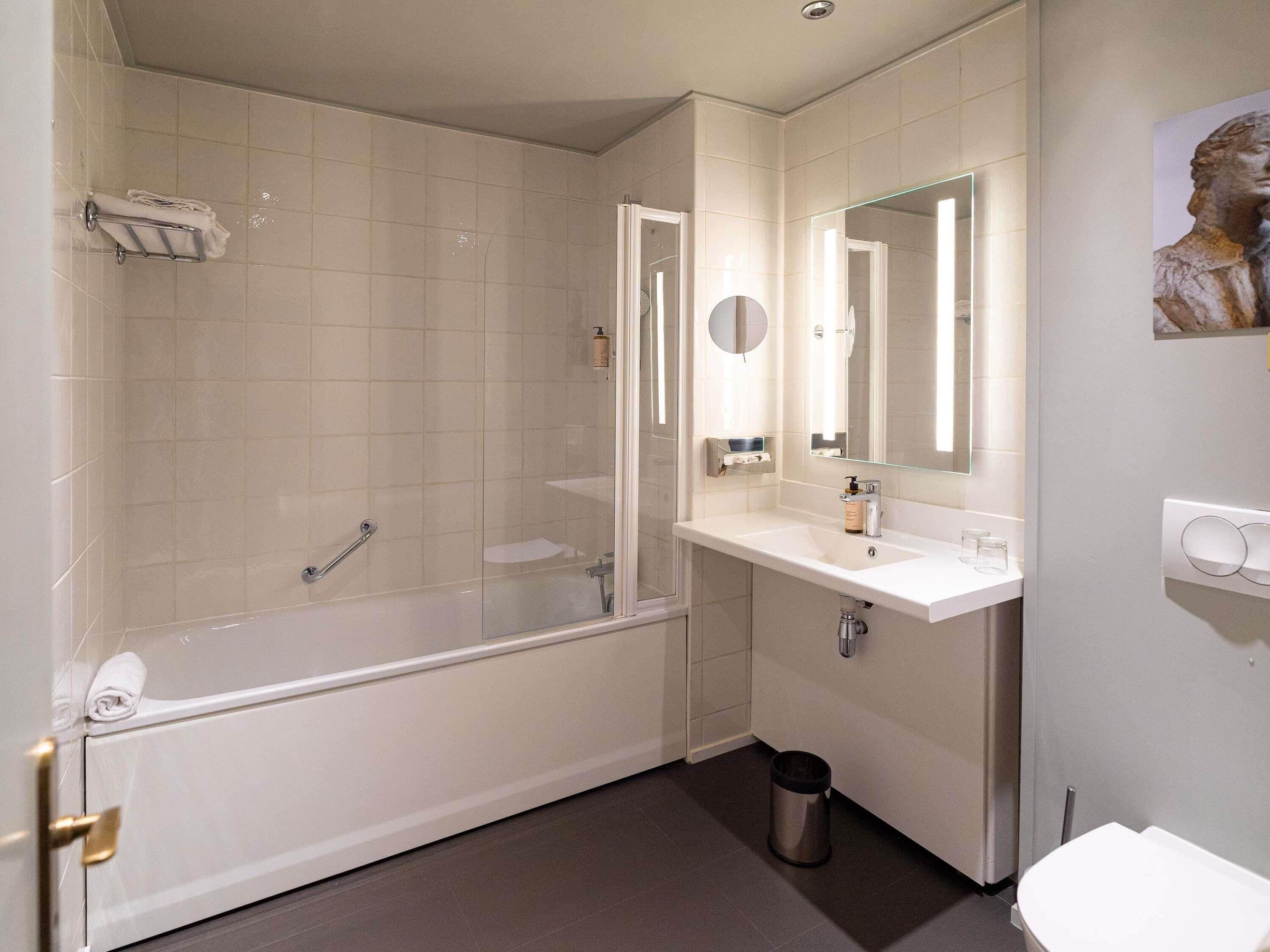 A bathroom with a bathtub, a sink, a mirror, and a toilet.