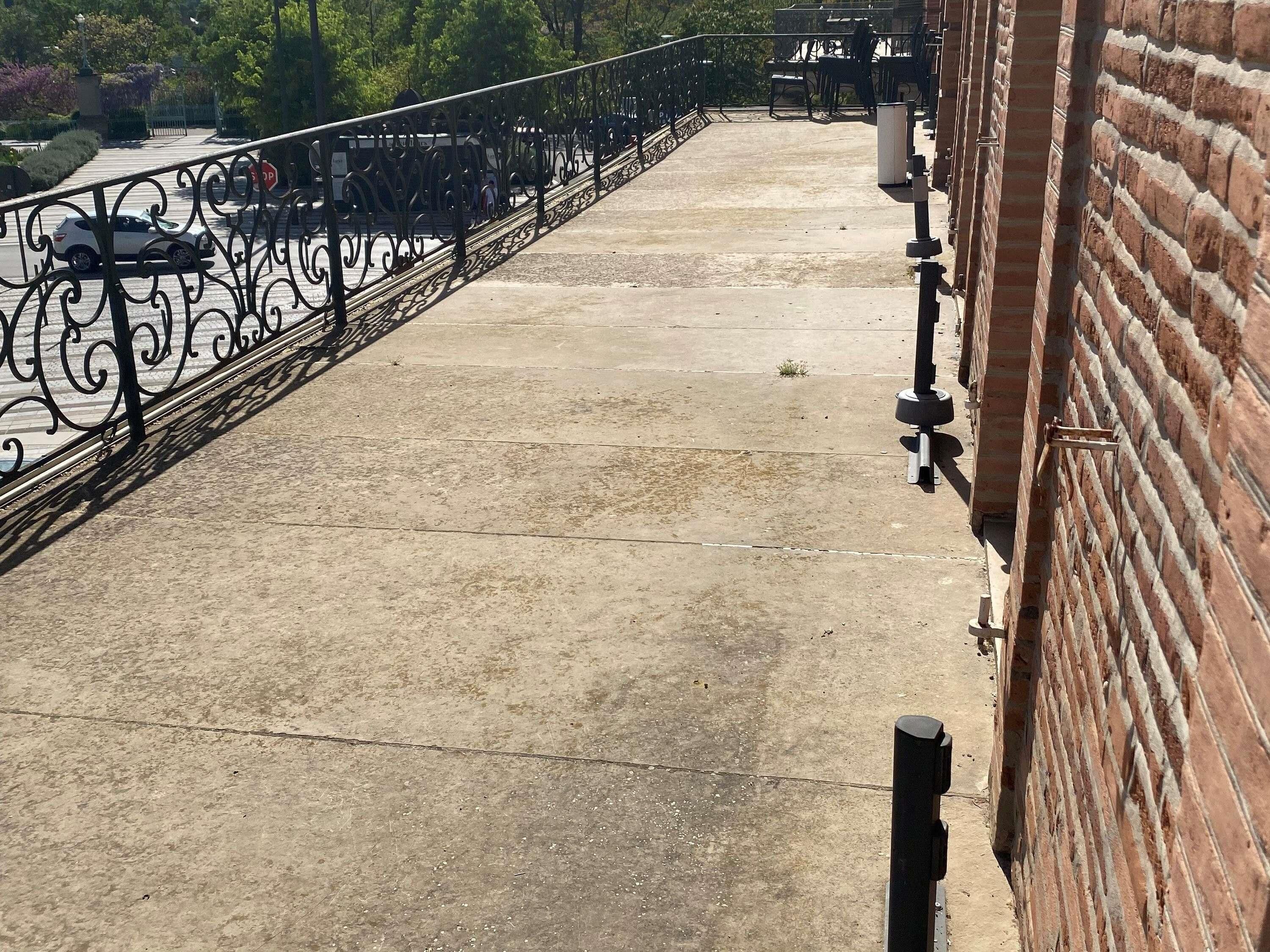 A concrete balcony with a metal railing, a brick wall, and a stop sign in the background.