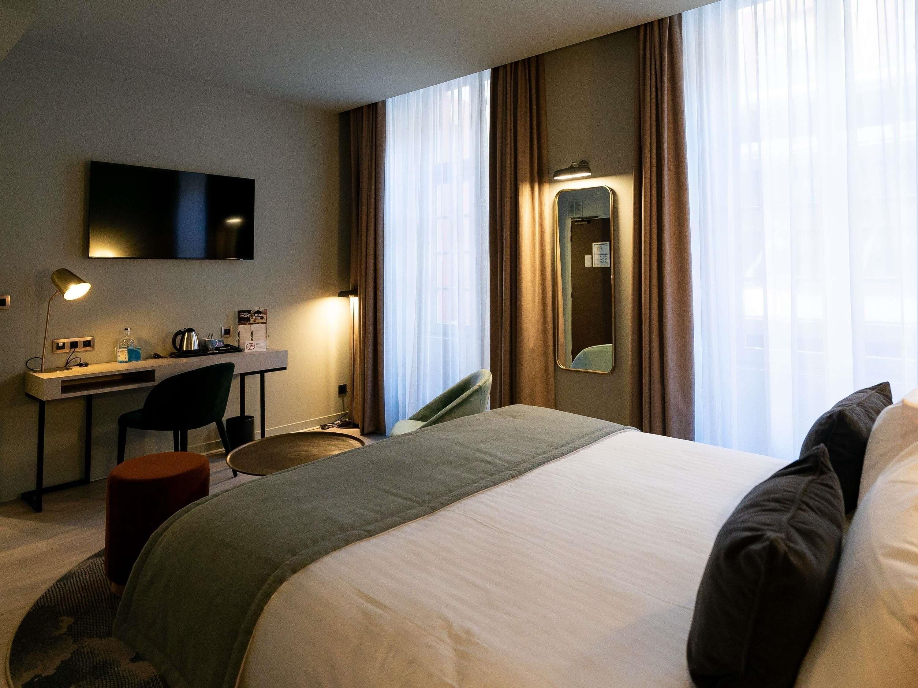 Habitación de hotel con cama, escritorio, silla y televisor montado en la pared.