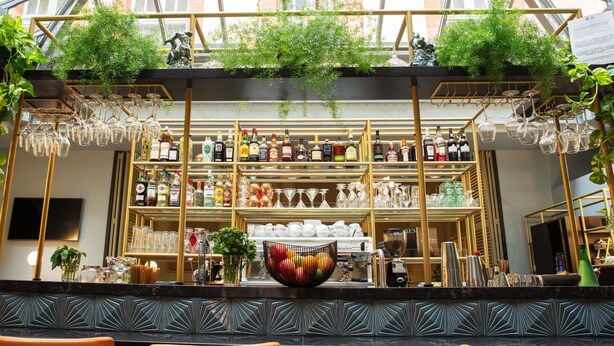 A bar area with shelves of liquor bottles and hanging wine glasses, a coffee machine, and a decorative bowl.