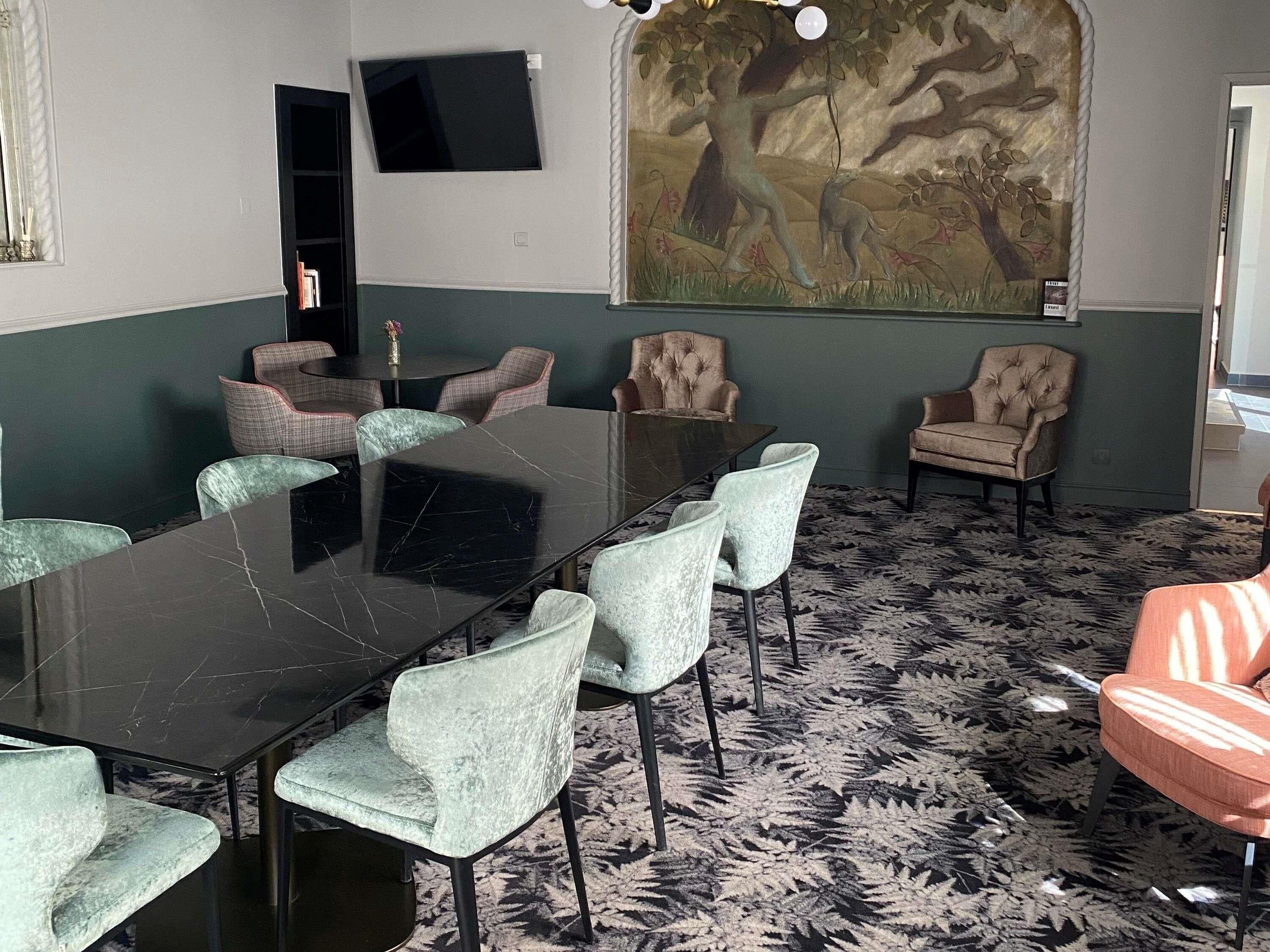 A conference room with a marble table, cushioned chairs, a large mural, and a television on the wall.