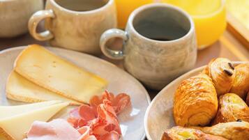 A breakfast tray with cheese, ham, croissants, and fruit.