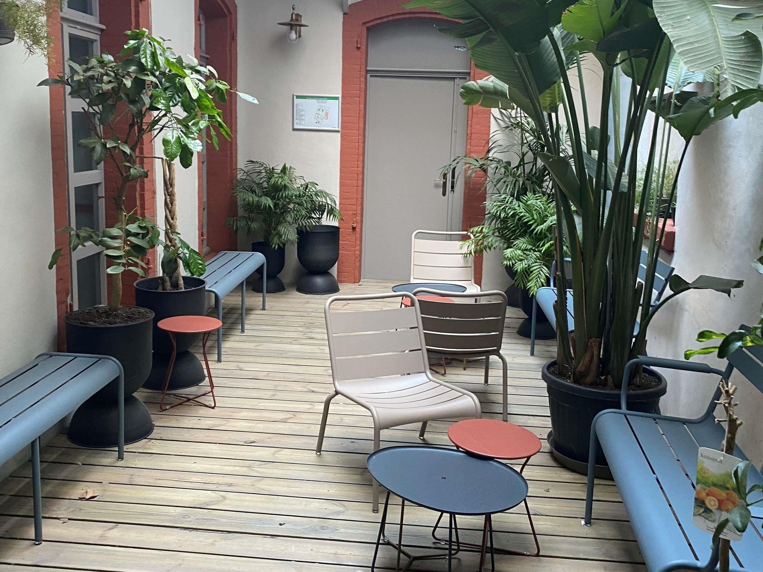 A wooden deck with metal chairs and tables, surrounded by potted plants and a red-framed door.