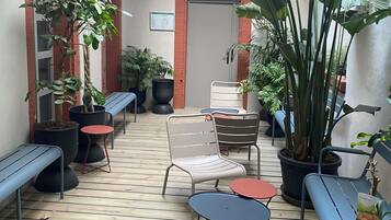 A wooden deck with metal chairs and tables, surrounded by potted plants and a red-framed door.