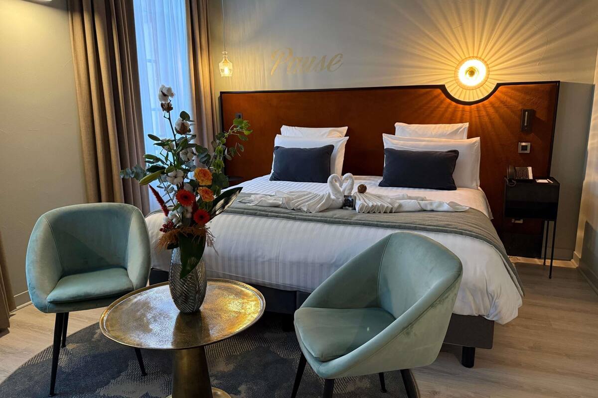 Ein Hotelzimmer mit einem Bett, zwei Sesseln, einem runden Tisch, einer Blumenvase, einer Wandleuchte und einem Schild mit dem Wort 'Place'.