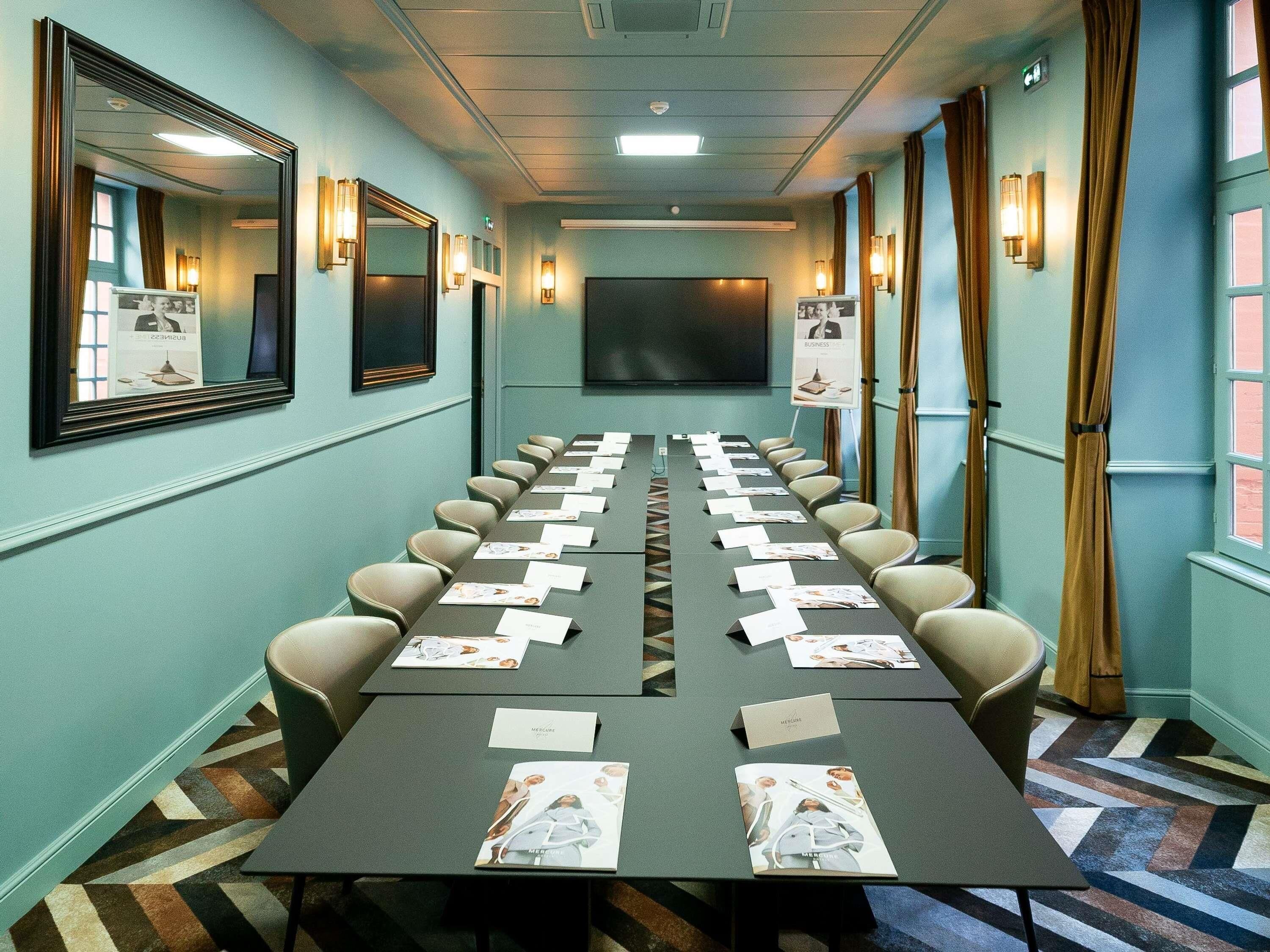 A conference room with a long table, chairs, name cards, and a projector screen.