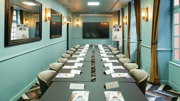 A conference room with a long table, chairs, name cards, and a projector screen.